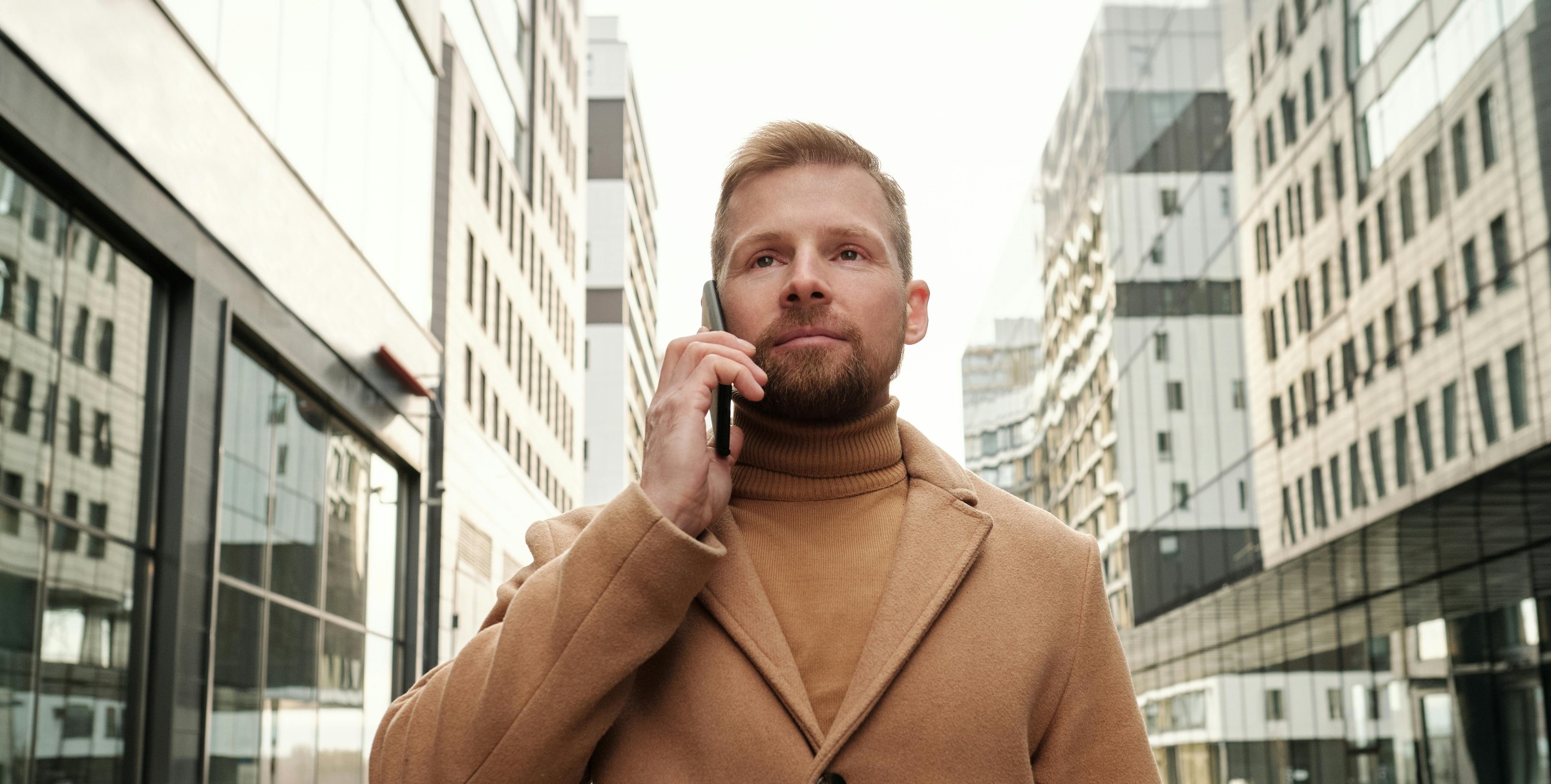 Man in a brown coat speaking on a phone in the centre of a city
